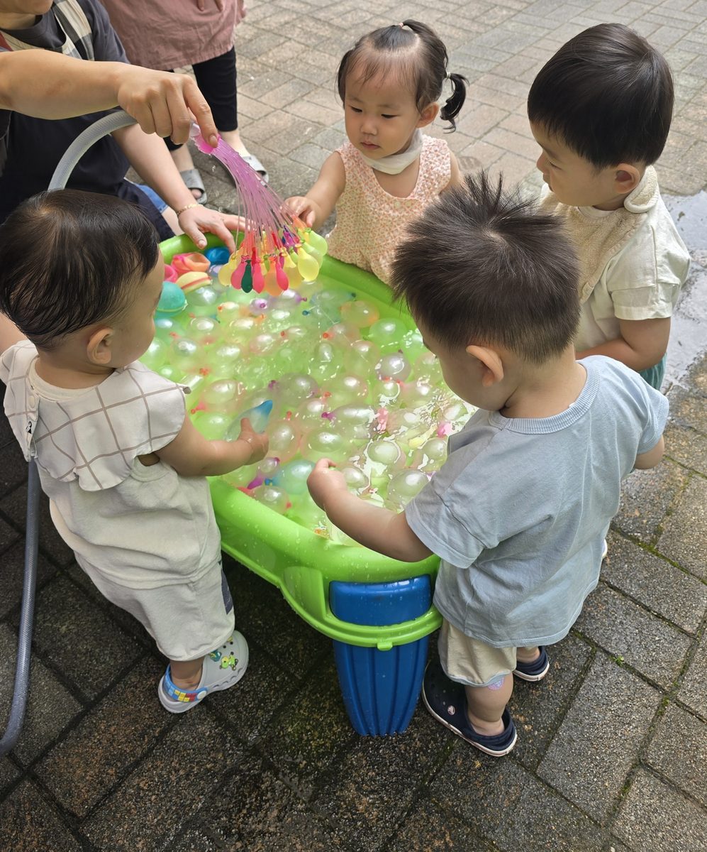 선생님이 들어 올린 물풍선 다발을 아이들이 함께 바라보는 모습